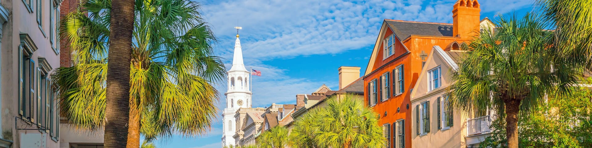 A street lined with palm trees and historic buildings, leading to a church with a steeple and clock tower.