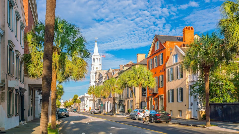 A street lined with palm trees and historic buildings, leading to a church with a steeple and clock tower.