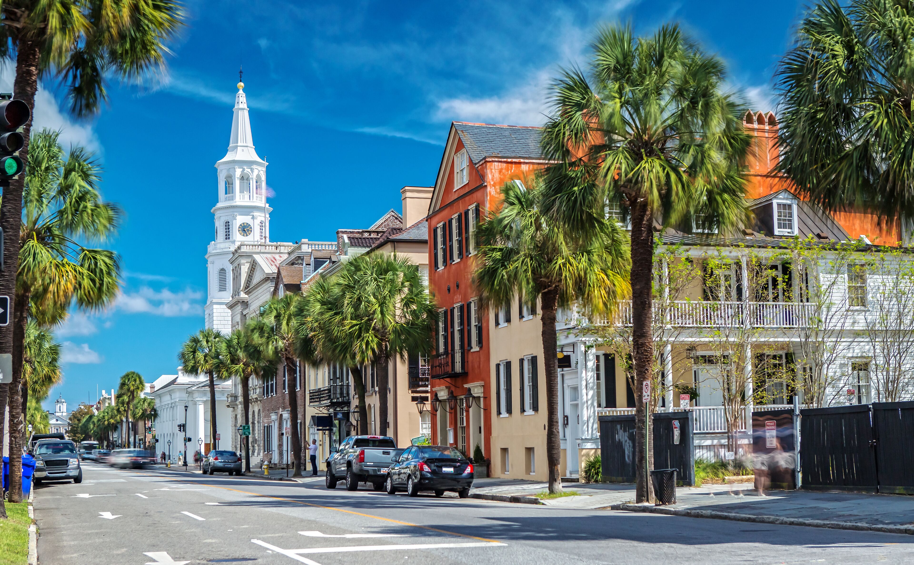 A street lined with palm trees, historic buildings, and a church tower.