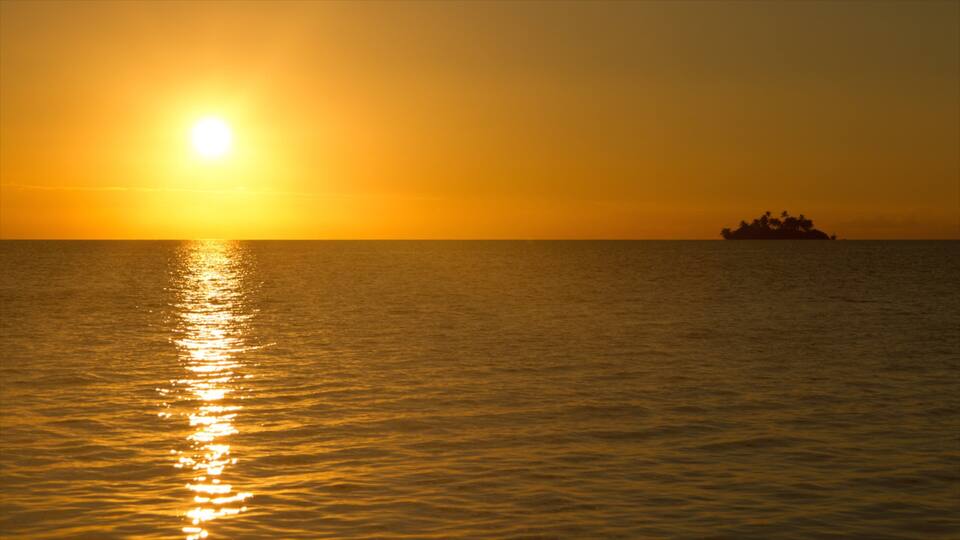 A sunset over the ocean with a boat in the distance.