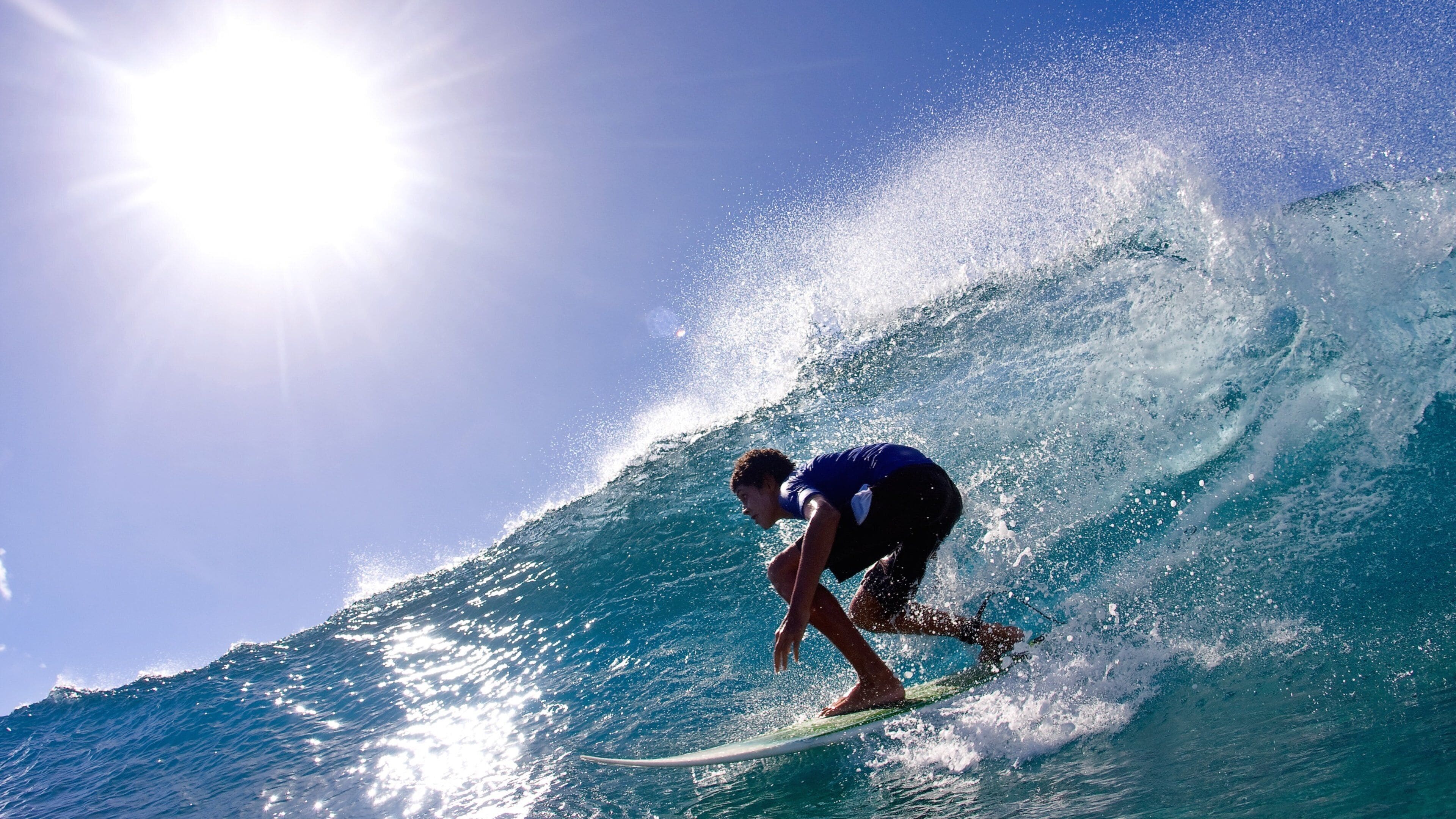 A surfer riding a wave with the sun shining in the background.