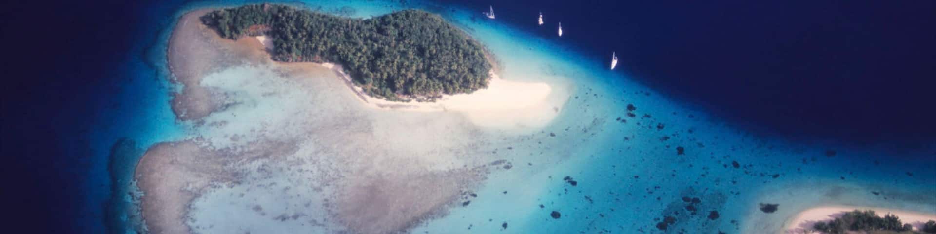 An aerial view of a tropical island with clear turquoise waters, a sandy beach, and a dense forested area.