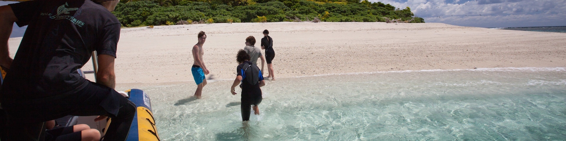 Una playa con agua turquesa cristalina, una orilla arenosa y una colina boscosa al fondo.