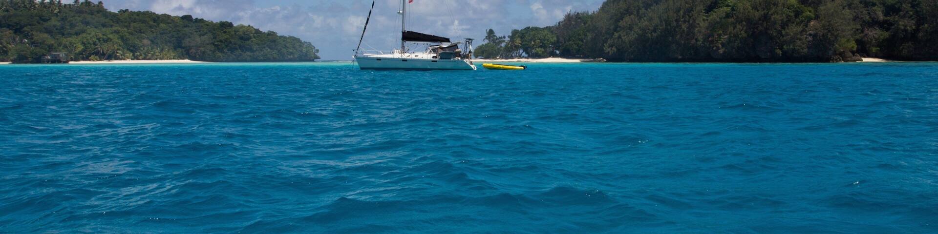 A sailboat on turquoise waters with a forested island in the background.