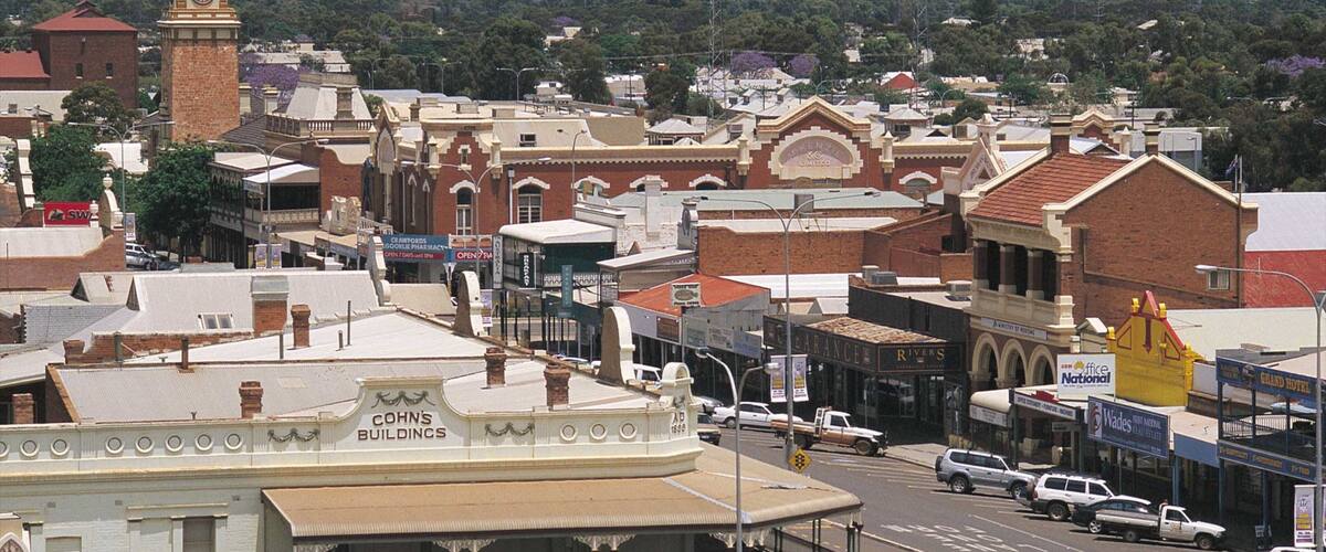 A historic town with a prominent clock tower, various commercial buildings, and a backdrop of green hills.
