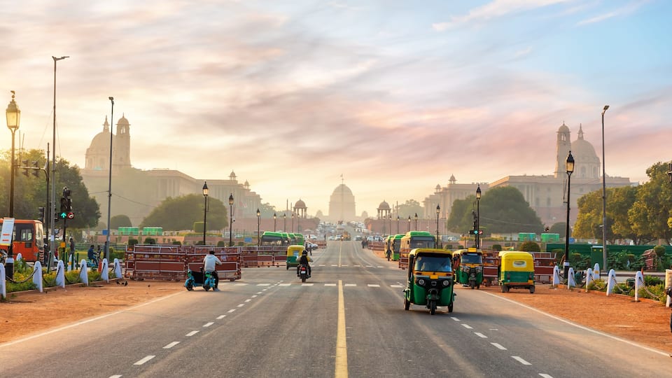 A busy urban road with auto-rickshaws, motorcycles, and buses.