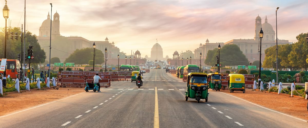 A busy urban road with auto-rickshaws, motorcycles, and buses.
