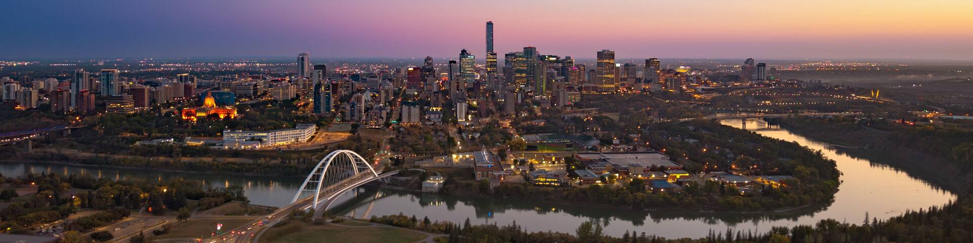 A city skyline at dusk with a prominent bridge and a river.