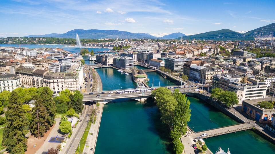 A cityscape with a river, a bridge, and mountains in the background.