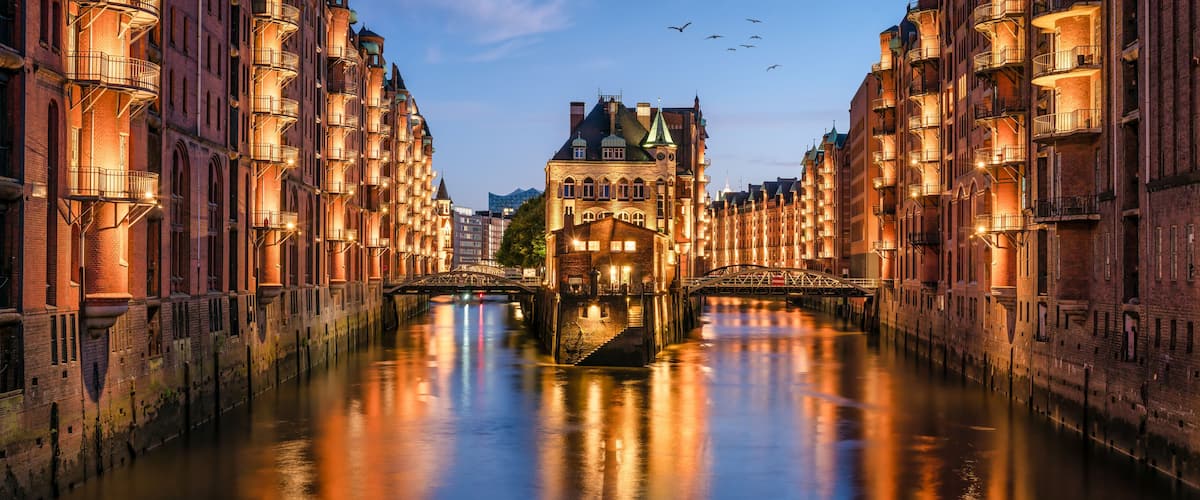A canal with buildings on either side, a bridge in the center, and a tower in the background.