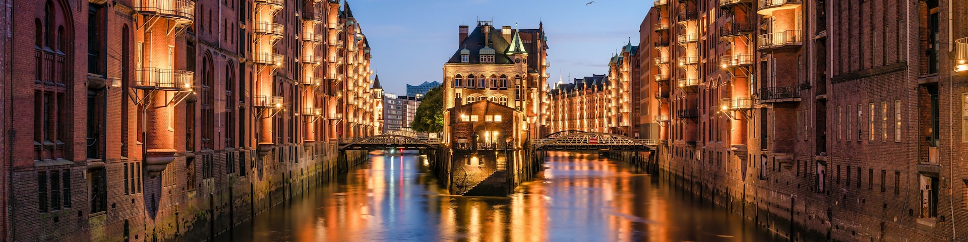 A canal with buildings on either side, a bridge in the center, and a tower in the background.