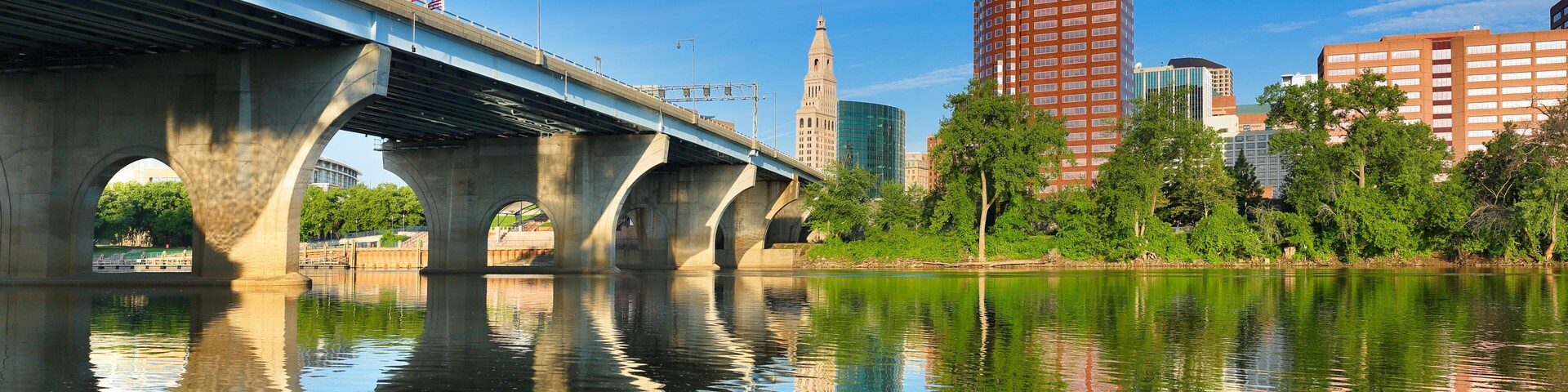 Uma ponte sobre um rio, com reflexos de edifícios e árvores.