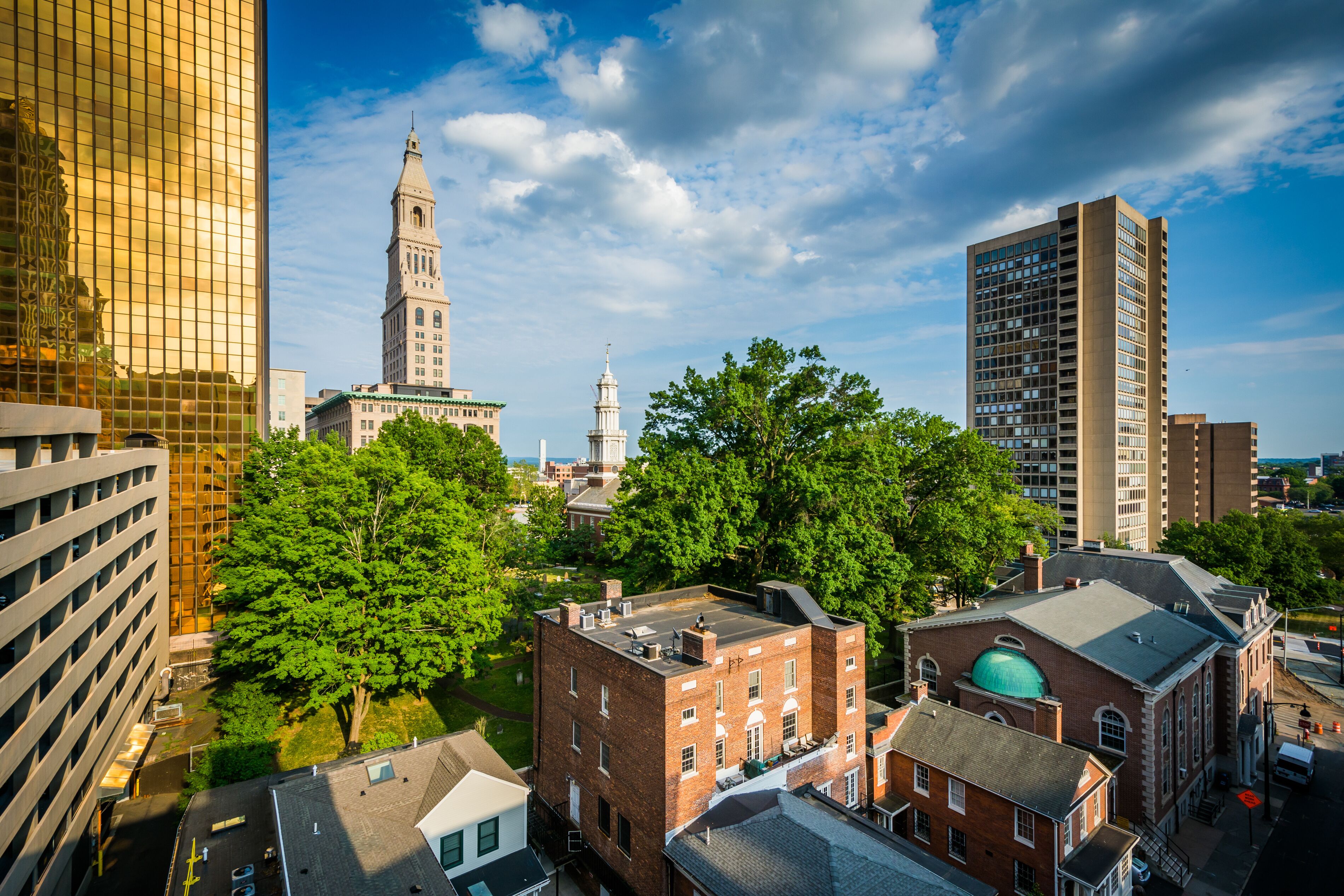 A cityscape with a mix of modern and historic buildings, including a prominent clock tower and a large green dome.
