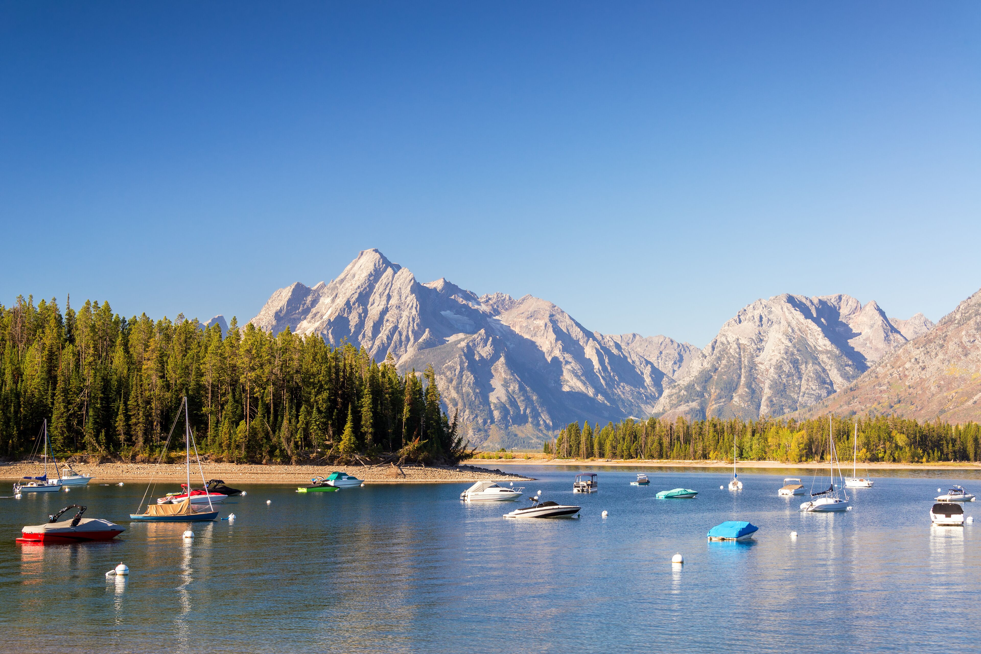 A lake with boats, surrounded by mountains and a forest.