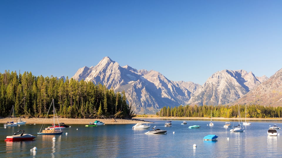 A lake with boats, surrounded by mountains and a forest.