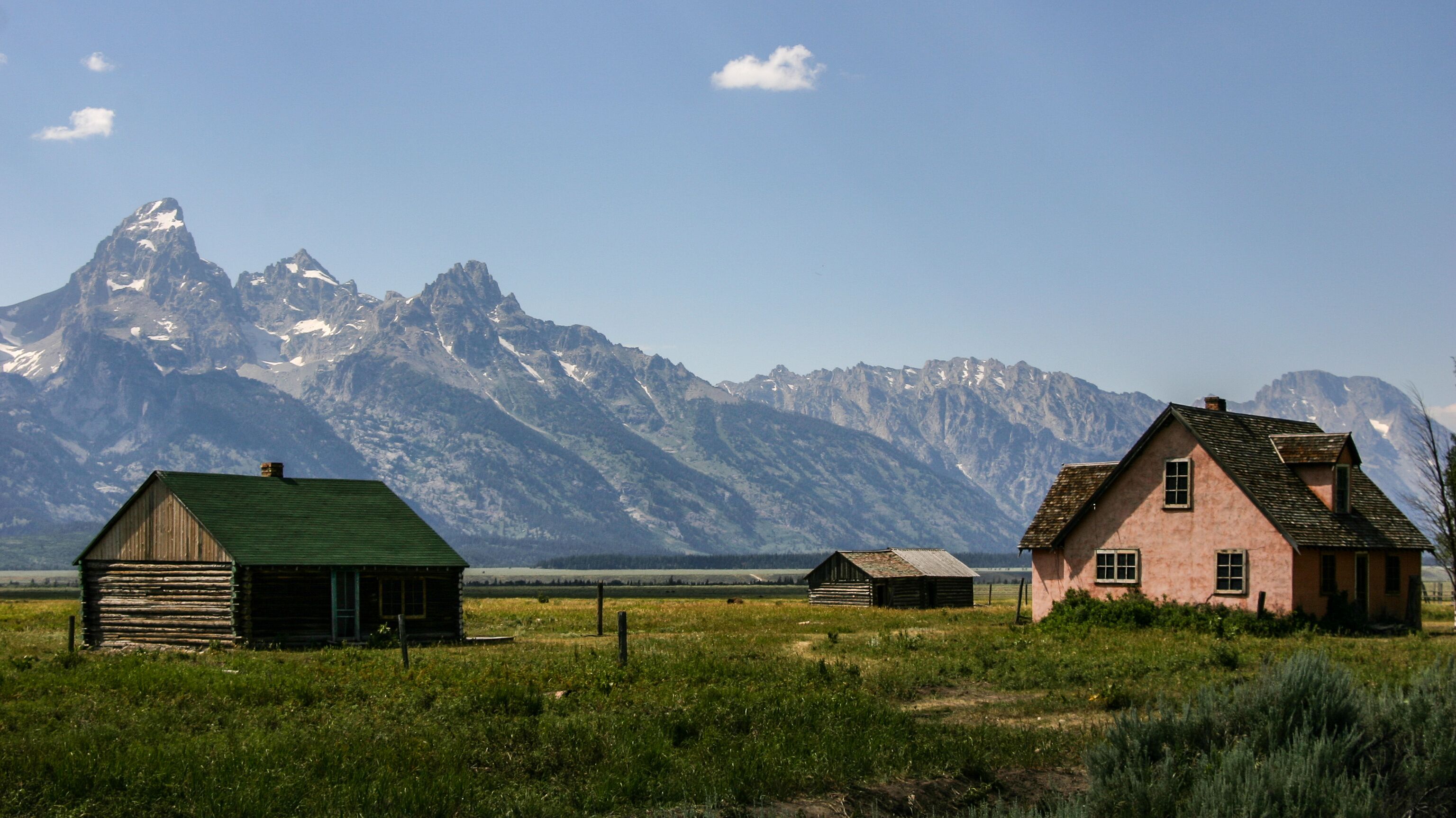 A rural landscape with two wooden houses and a mountain range in the background.