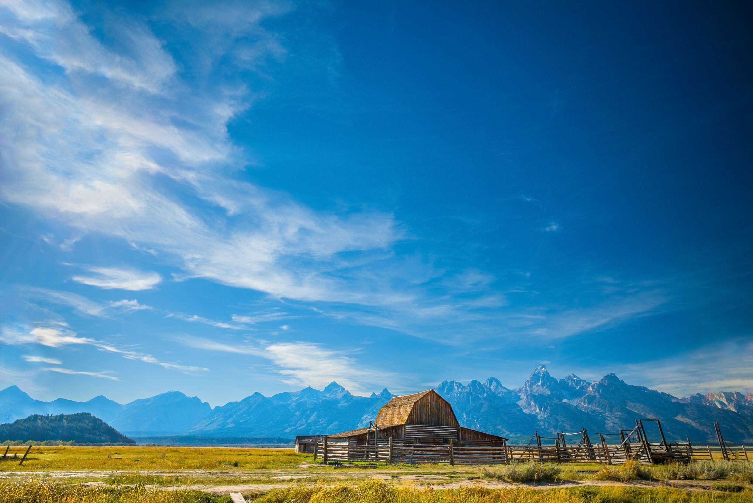 A wooden barn in a grassy field with mountains in the background.