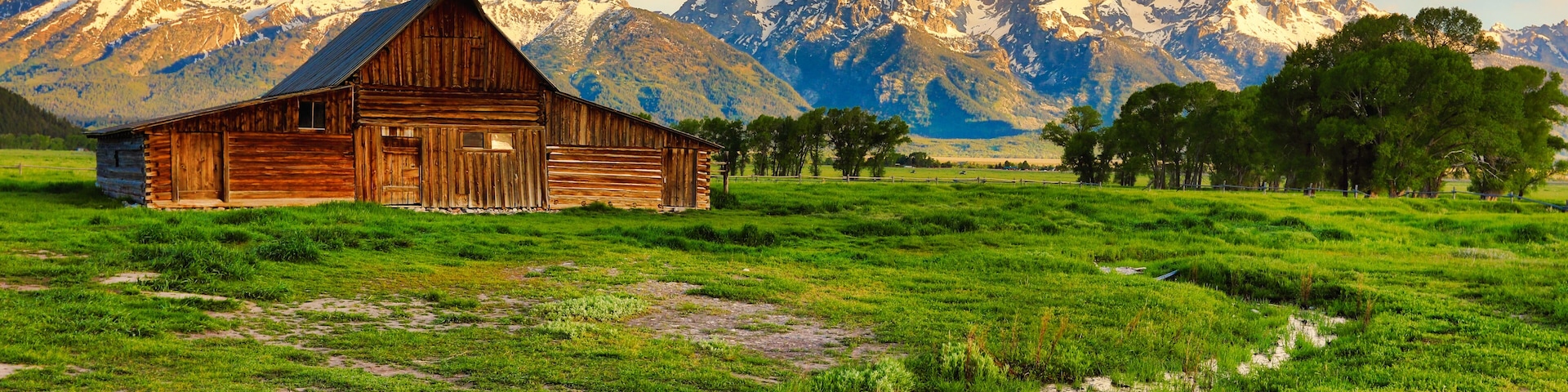 A wooden barn in a grassy field with a mountain range in the background.