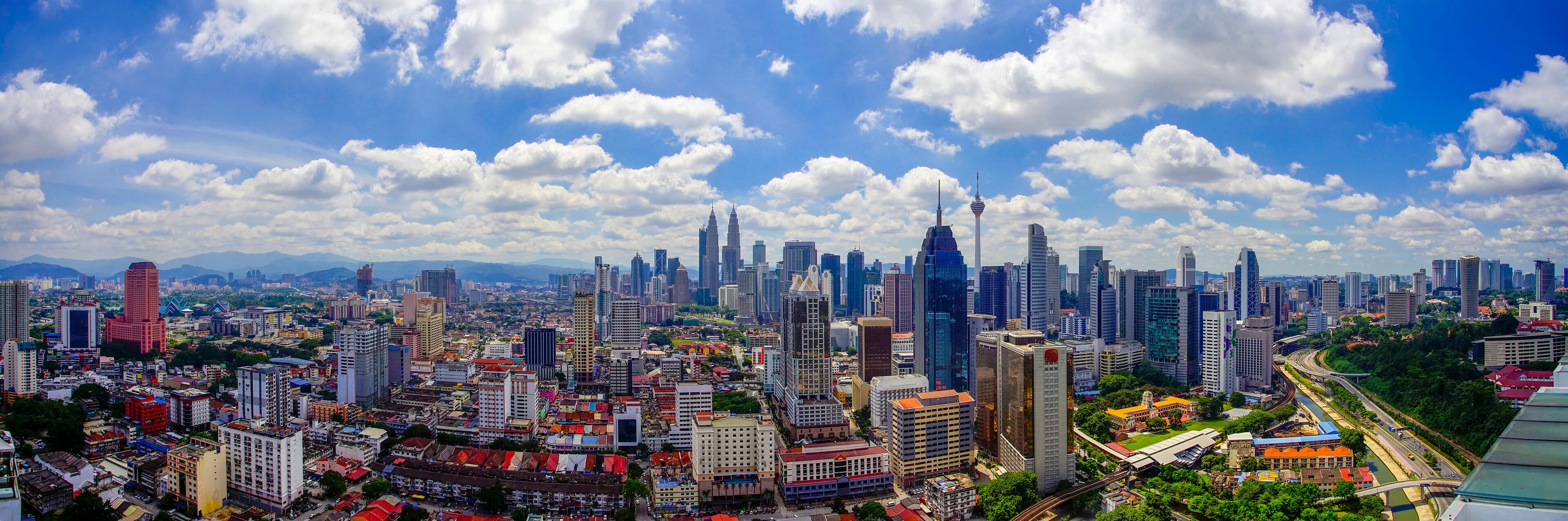 Panorama view of Kuala Lumpur city skyline with dramatic cloud formation and blue sky.