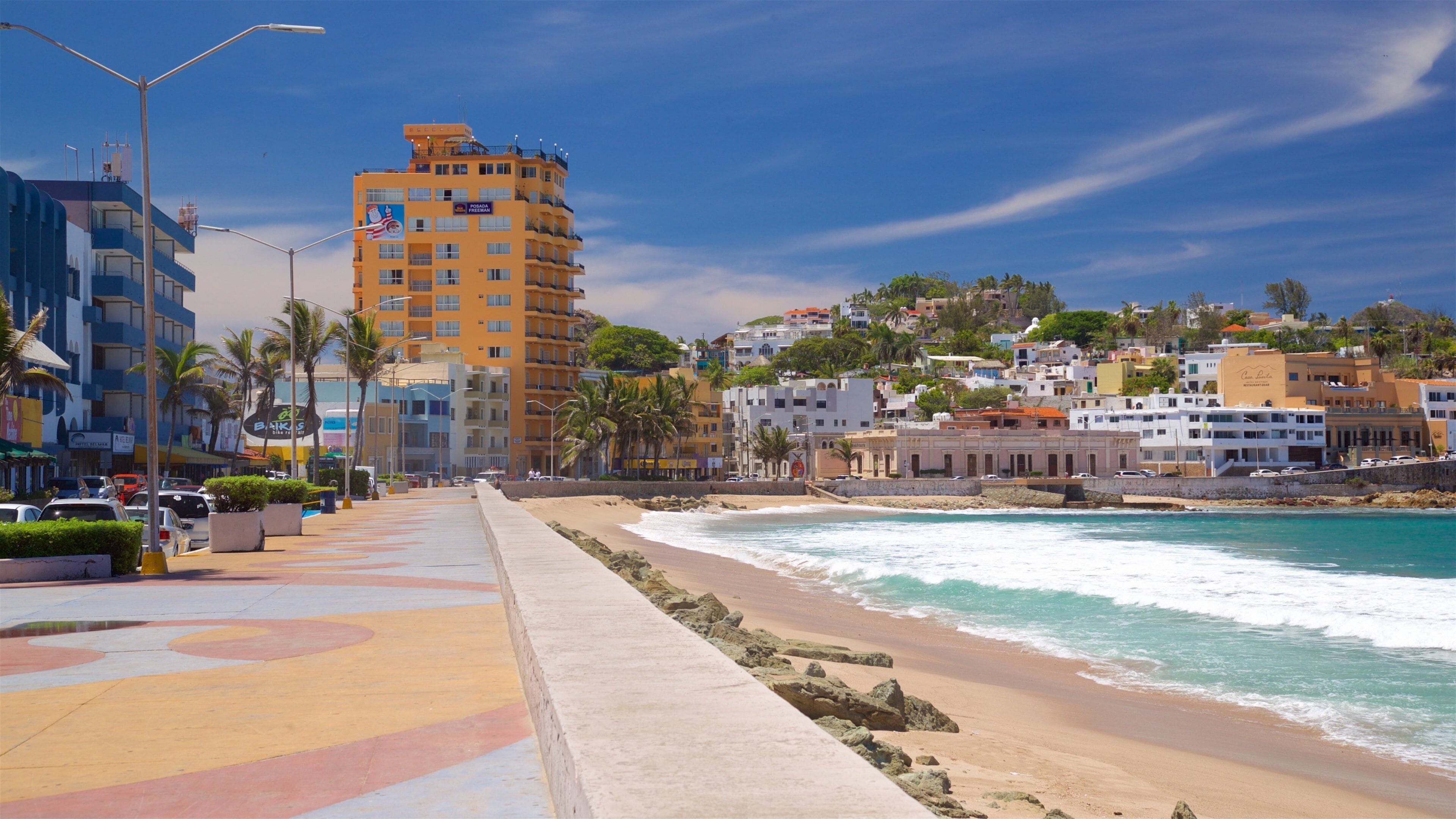Paisagem costeira com praia, palmeiras e edifícios coloridos.