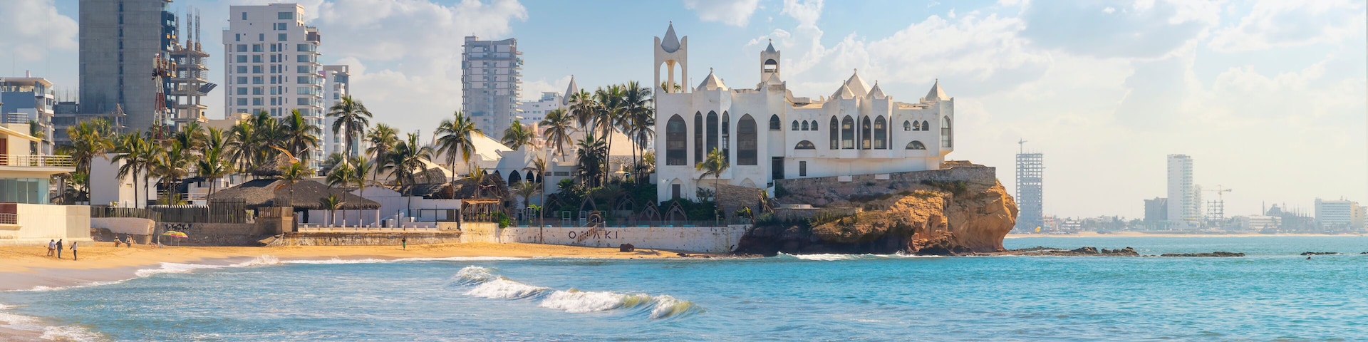 A coastal cityscape with a prominent white church, palm trees, and modern buildings.