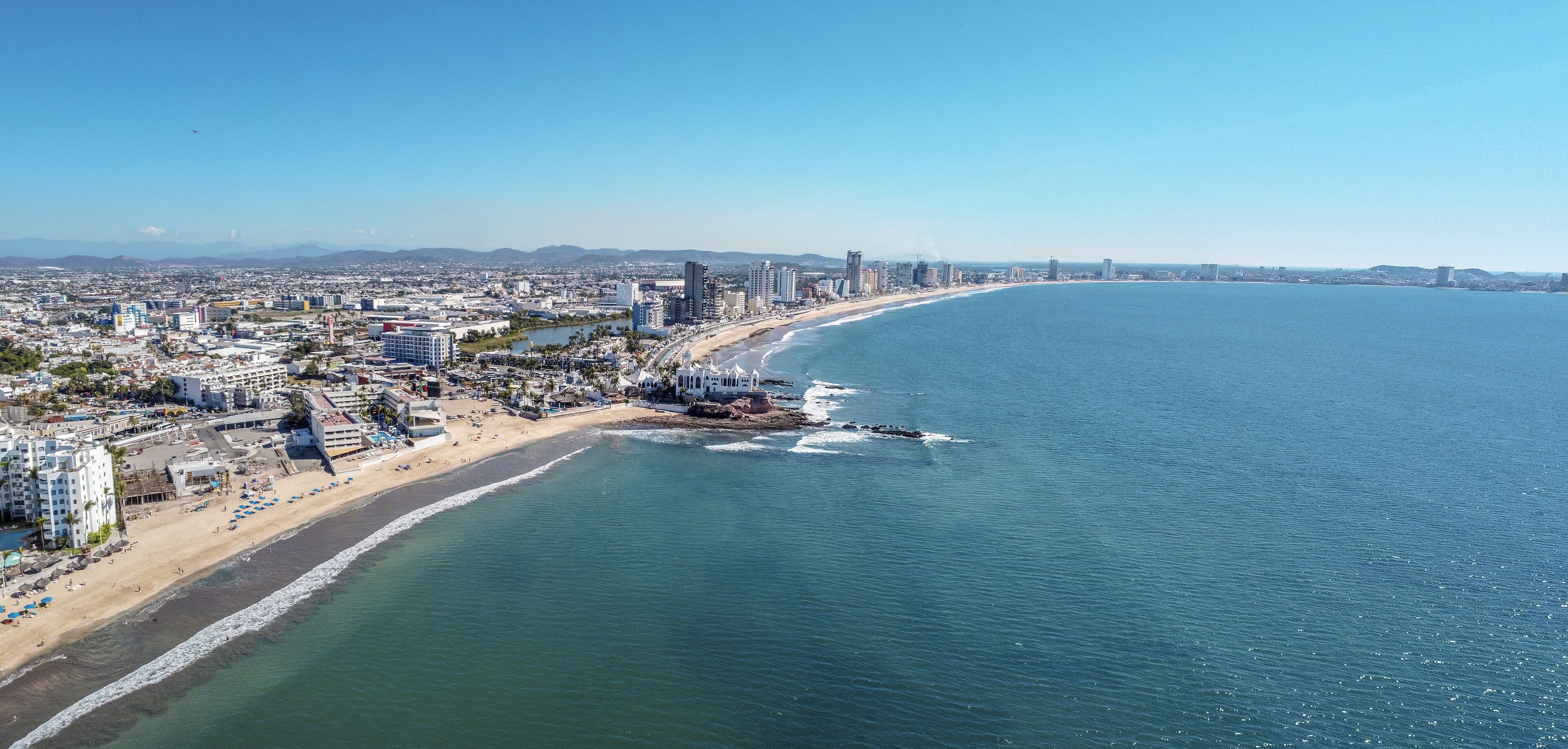 A coastal cityscape with a beach, buildings, and a clear blue sky.