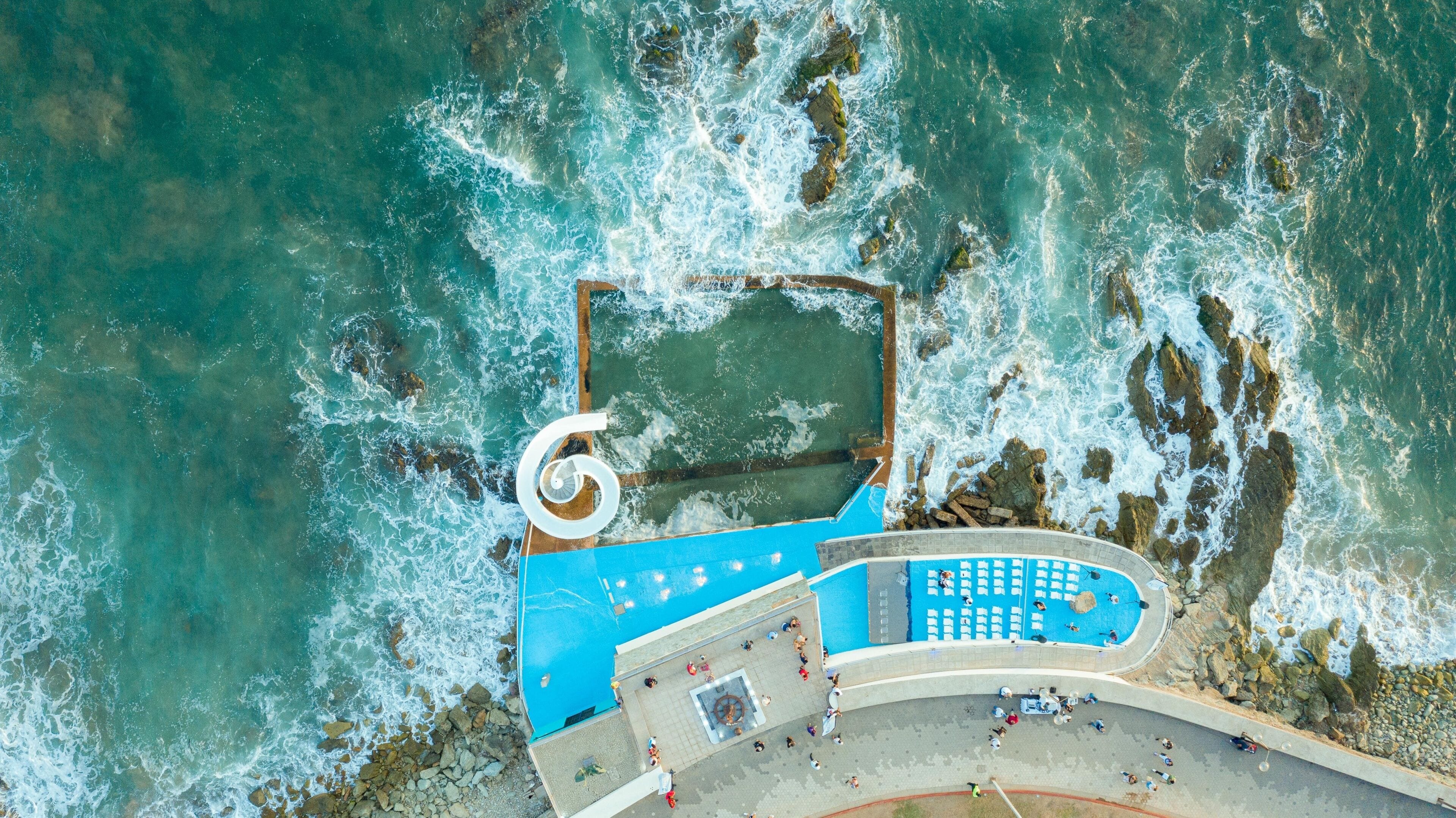 Vista aérea de una zona costera con una amplia piscina azul, costa rocosa y una estructura circular.