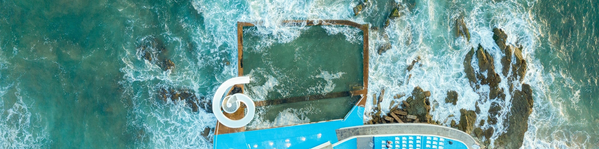 Vista aérea de una zona costera con una amplia piscina azul, costa rocosa y una estructura circular.