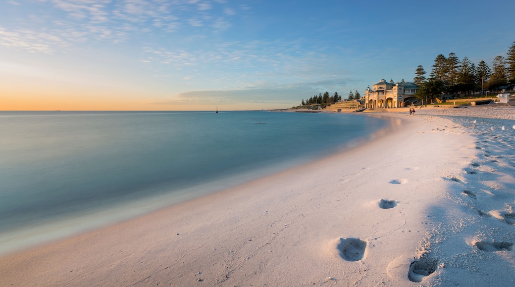 A beach with footprints, a calm sea, and a building with a dome on the shore.