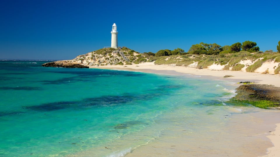 A lighthouse on a rocky outcrop, clear turquoise waters, and a sandy beach.