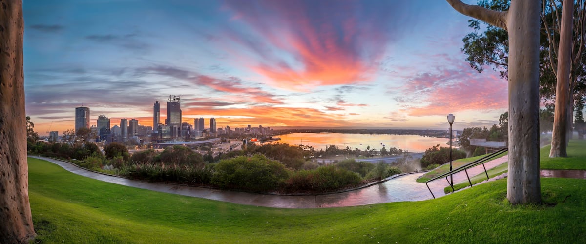 A city skyline at sunset with a river in the foreground.