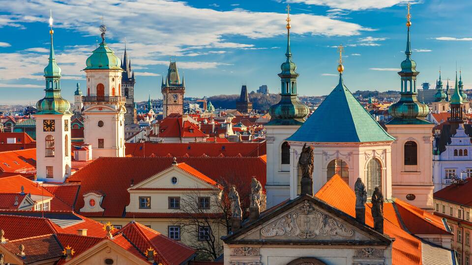 A cityscape with red-roofed buildings, green domes, and a clock tower.