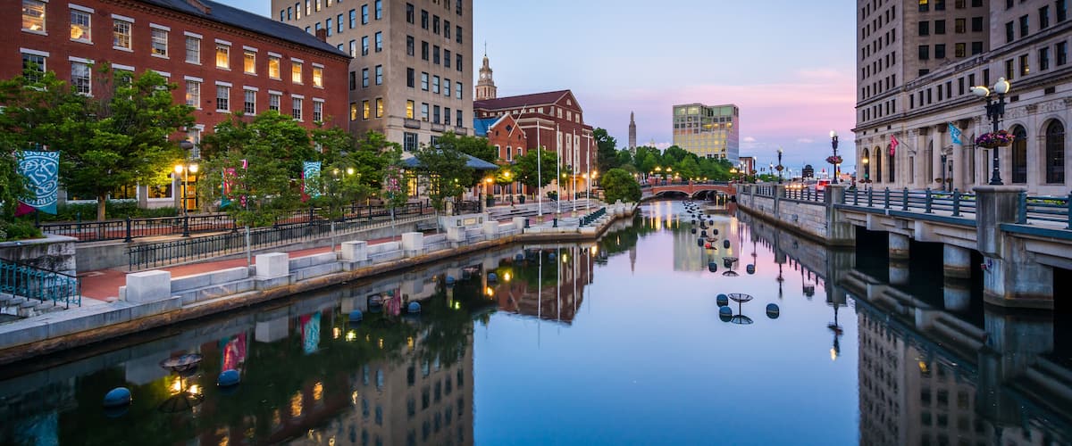 A calm river reflecting buildings, a bridge, and a historic building with a clock tower.