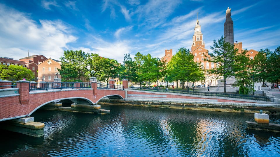 A river with a bridge, a tall tower, and a building with a clock tower.