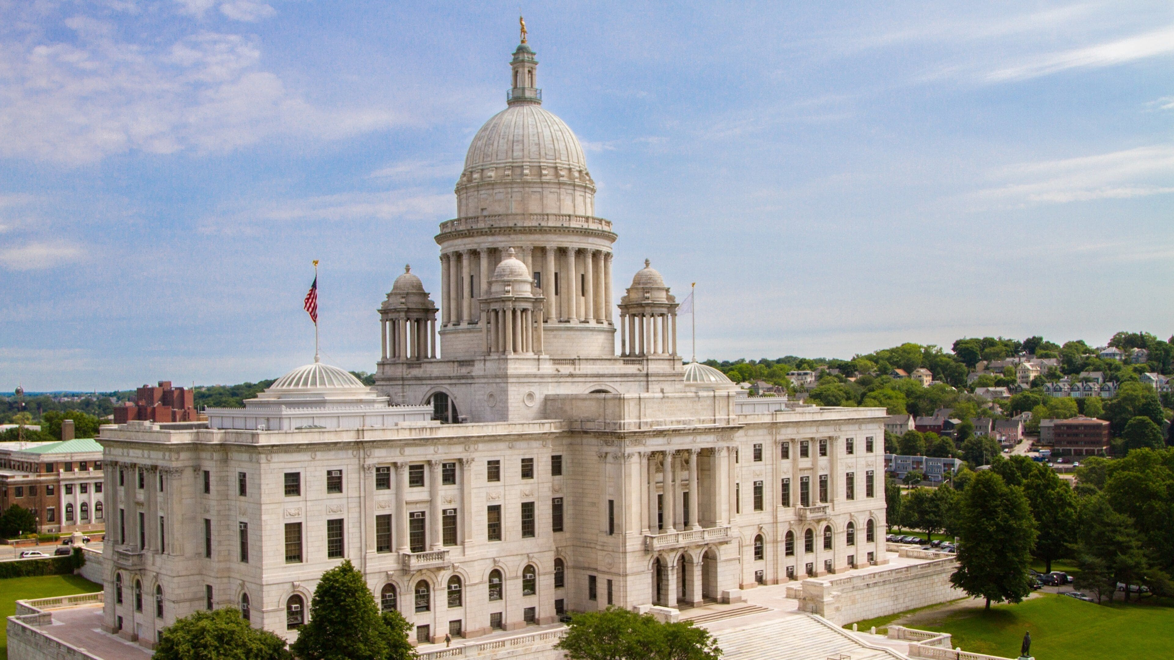 A large neoclassical building with a prominent dome and columns, surrounded by greenery and a clear sky.