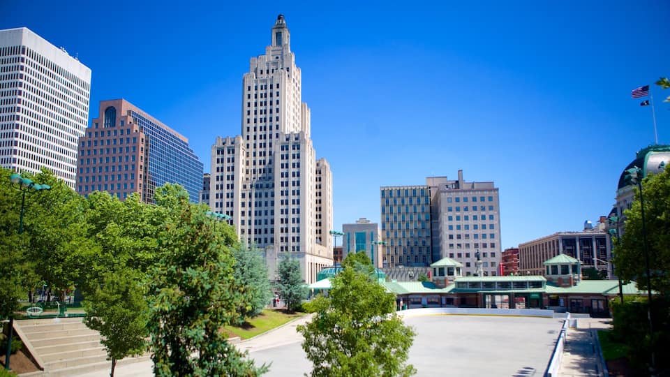 A cityscape with modern and historic buildings, a clear blue sky, and green trees.