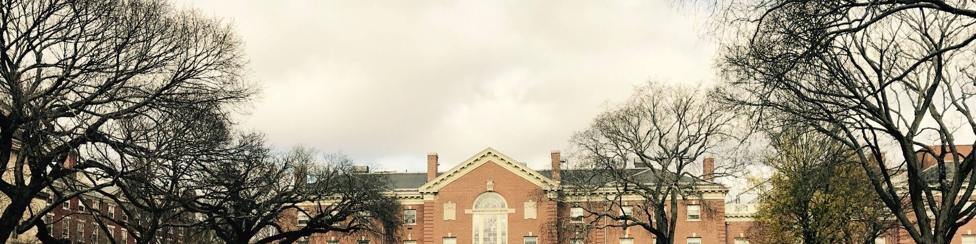 A large brick building with a central entrance, surrounded by a grassy field and leaf-covered ground.