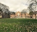 A large brick building with a central entrance, surrounded by a grassy field and leaf-covered ground.