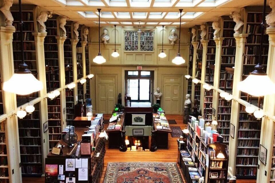 A library interior with bookshelves, a central reading area, and decorative statues.