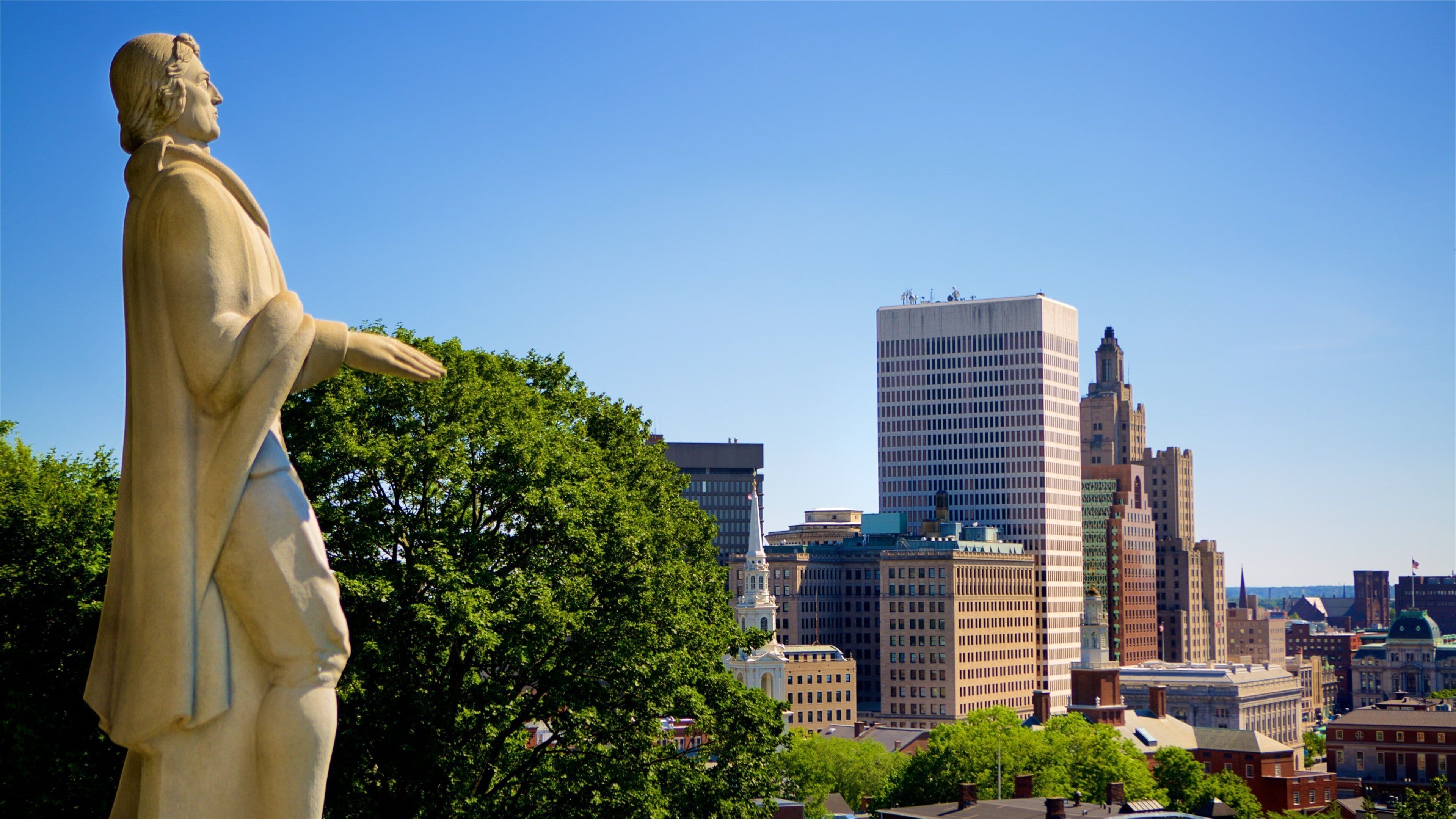 A statue in a park with a cityscape in the background.