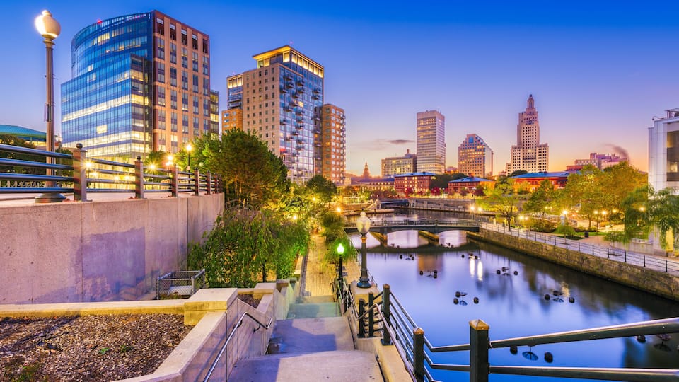 A cityscape with a river, modern buildings, and a bridge at dusk.