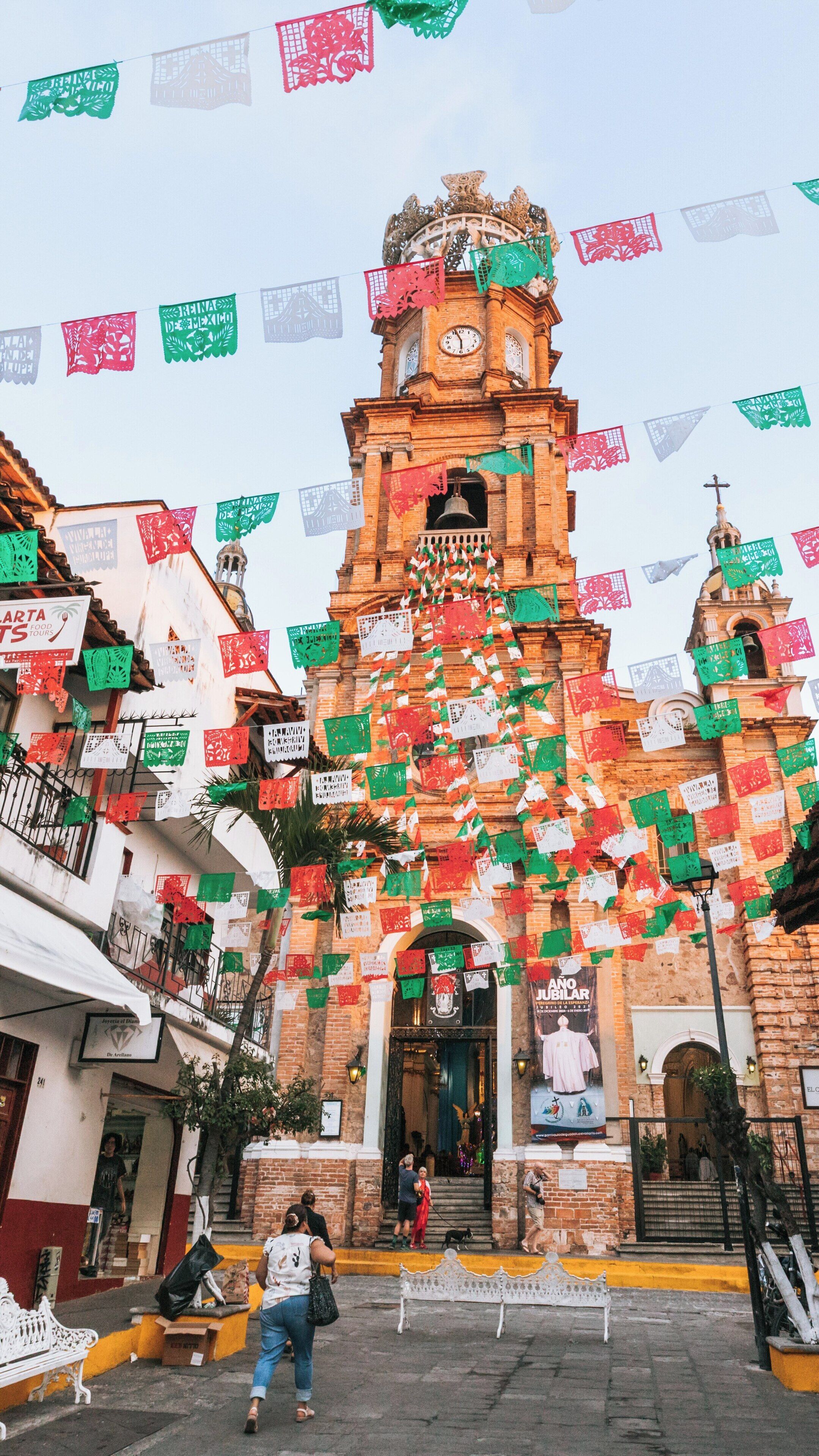 Explore the beauty of Church of Our Lady of Guadalupe in Downtown Puerto Vallarta, Mexico, adorned with colorful papel picado decorations during a vibrant celebration