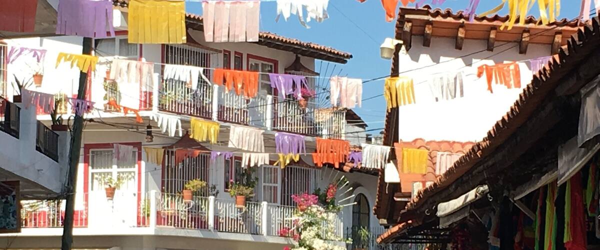 A street with colorful laundry hanging from balconies, parked cars, and a flower display.
