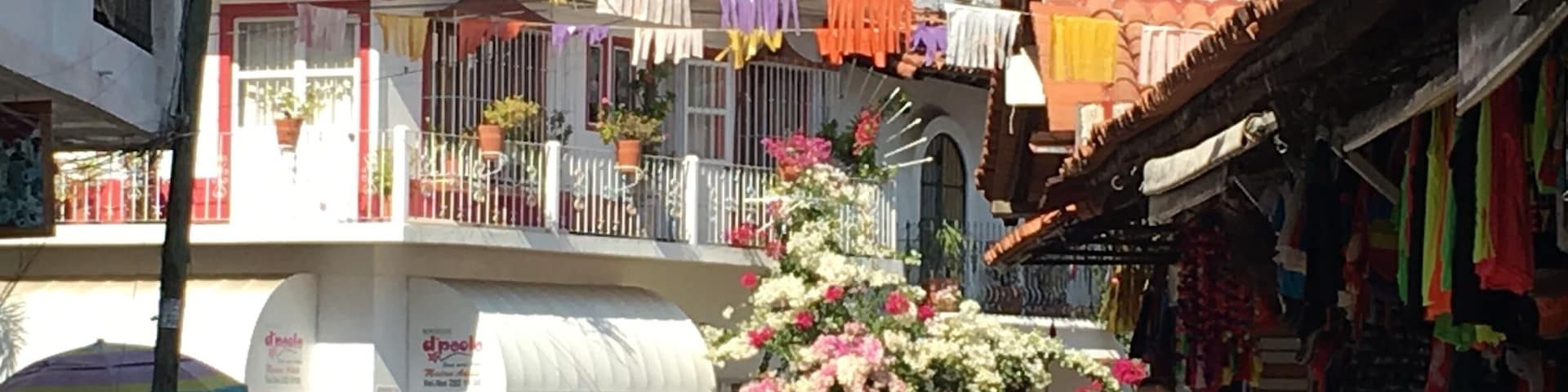 A street with colorful laundry hanging from balconies, parked cars, and a flower display.