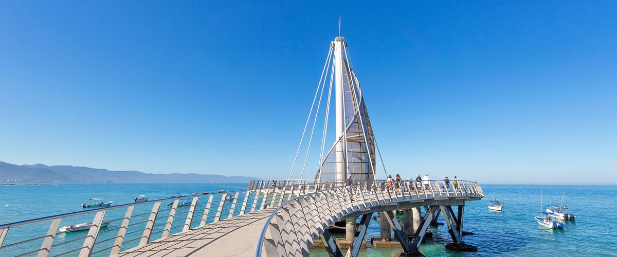 Un puente moderno con un diseño único, que se extiende sobre un mar tranquilo con barcos cerca.