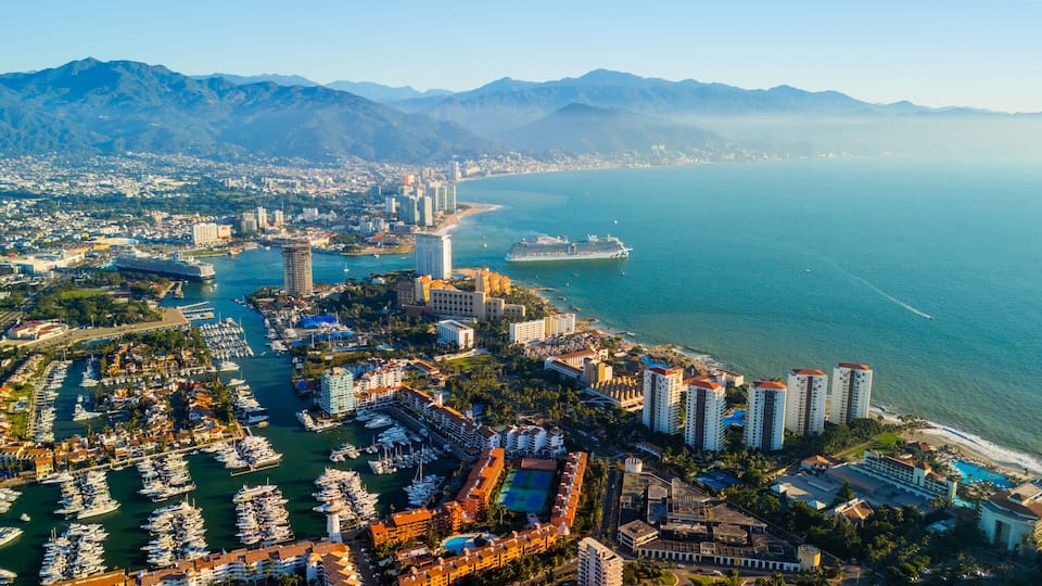 Un paisaje urbano costero con un puerto deportivo, rascacielos y un crucero.