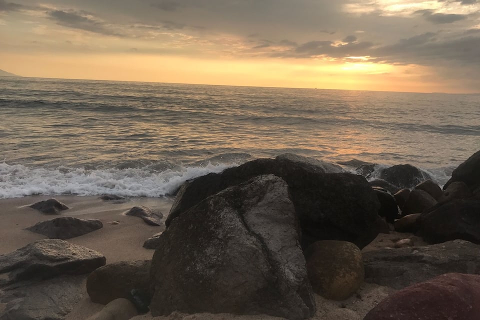 Ein felsiger Strand bei Sonnenuntergang, Wellen im Wasser.