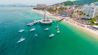 A coastal city with a prominent bridge connecting two land masses, a beach with umbrellas, and several boats in the water.