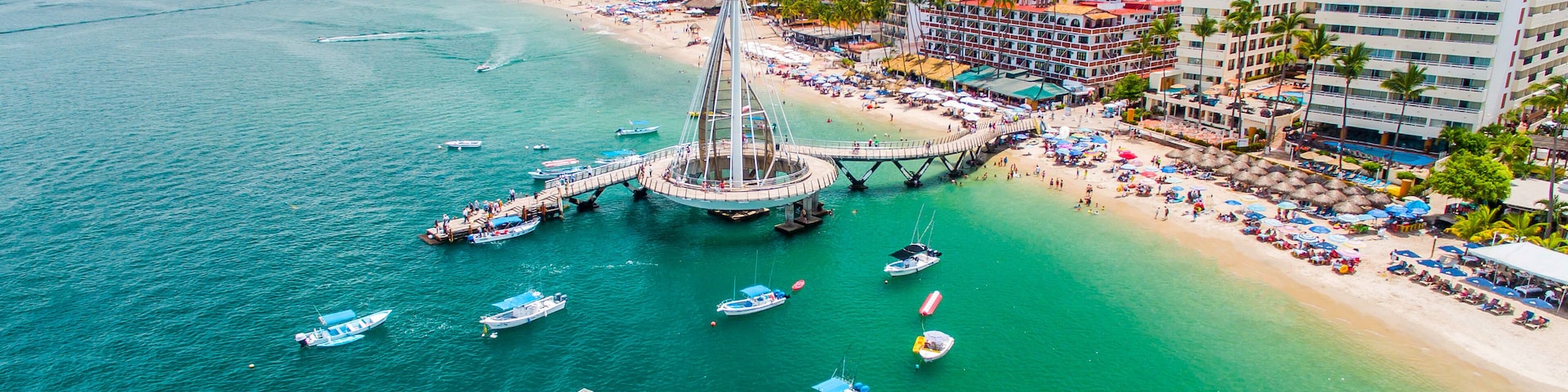 A coastal city with a prominent bridge connecting two land masses, a beach with umbrellas, and several boats in the water.