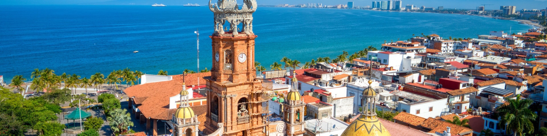 Un paisaje urbano costero con una imponente torre de iglesia y un edificio de cúpula dorada.